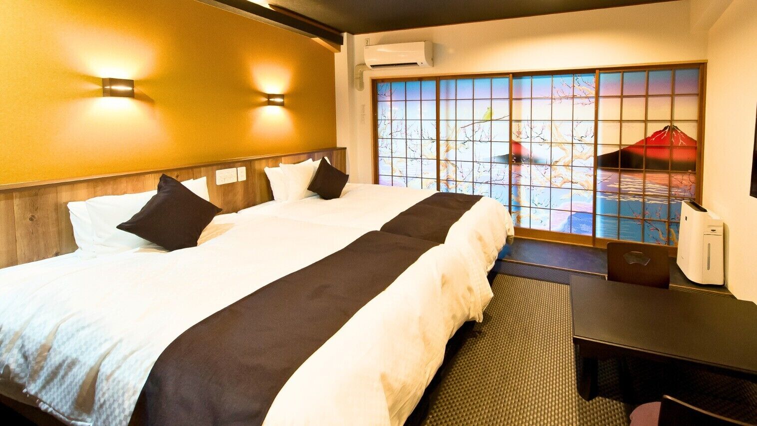 Habitación de hotel con una cama grande, dos lámparas de pared, vistas a través de una ventana con un panel decorativo y un escritorio con una silla.