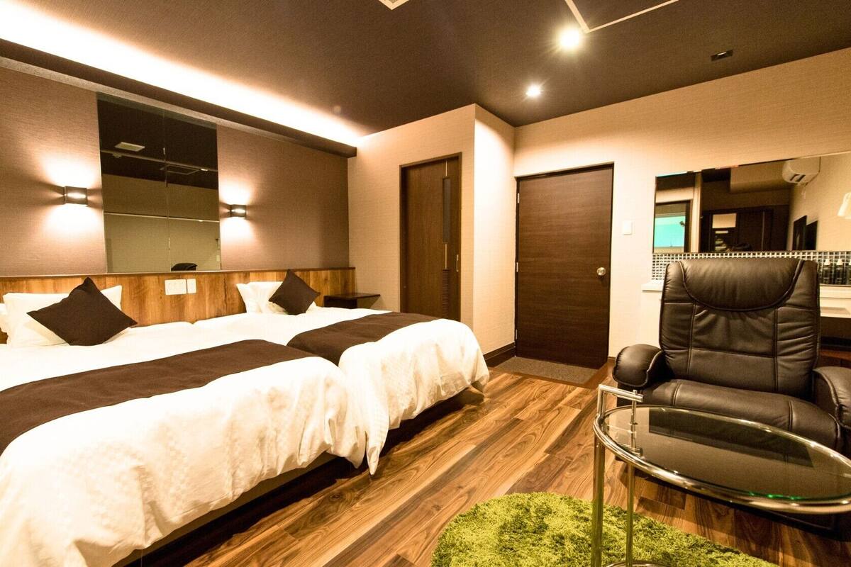 A hotel room with two beds, a mirror, a chair, and a small table.