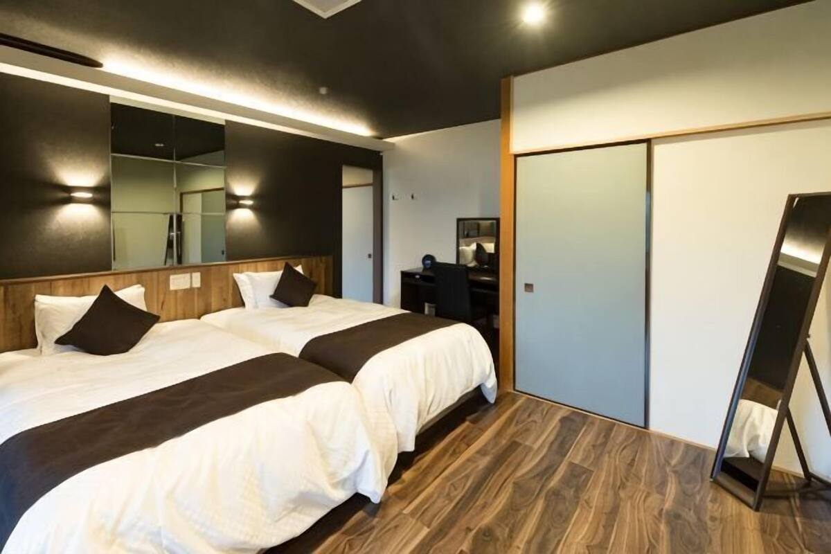 A hotel room with two beds, a large mirror, a wardrobe, and a desk.