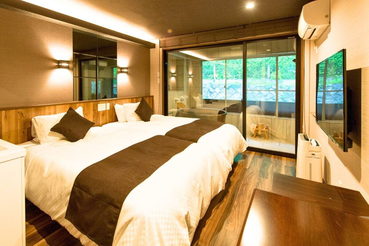 A modern hotel room with a large bed, a desk, and a glass door leading to a balcony.