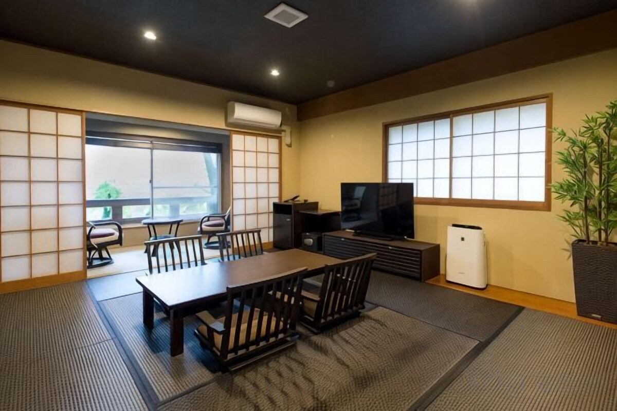 Una habitación de estilo japonés tradicional con suelo de tatami, una mesa baja con cojines, un televisor y una planta en maceta.