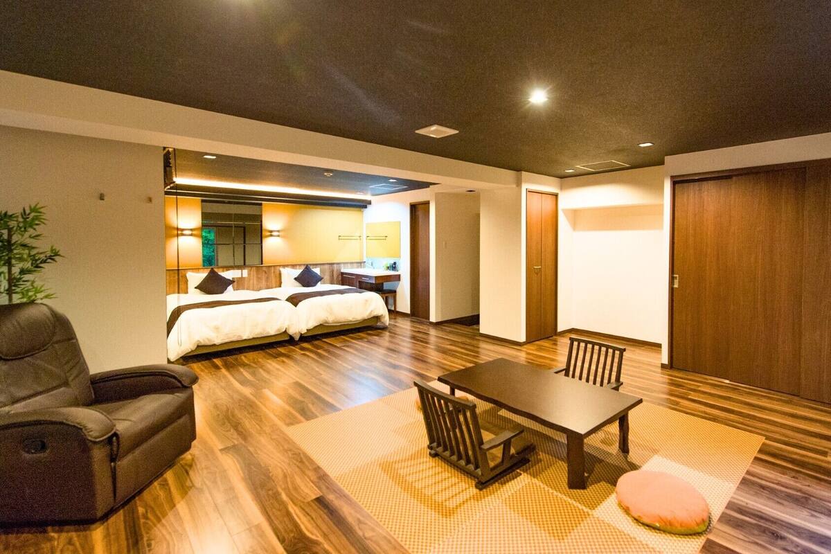 A hotel room with a bed, a sofa, a dining table, and a wooden floor.