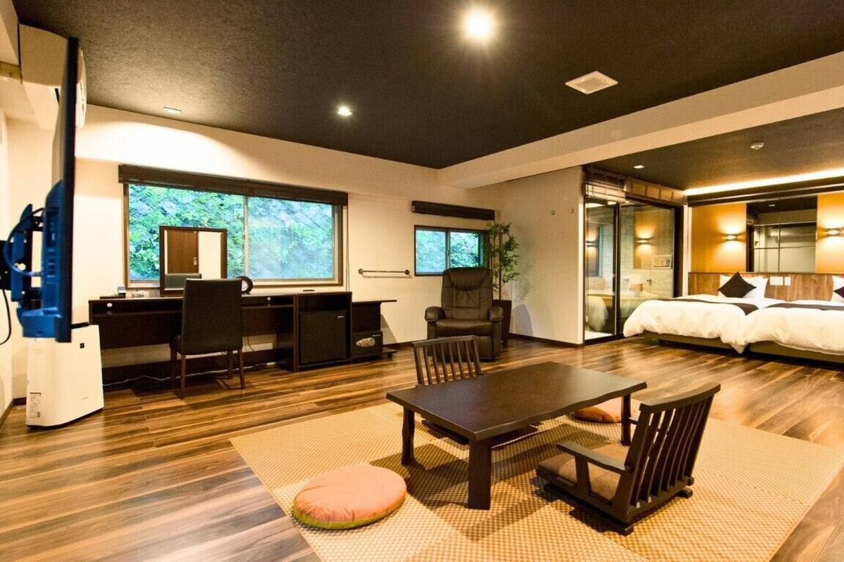A modern hotel room with a desk, chair, bed, and large windows.