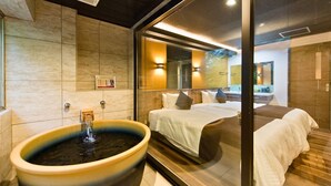 Un baño moderno con una bañera grande, una cama con ropa blanca y un box de ducha de vidrio.