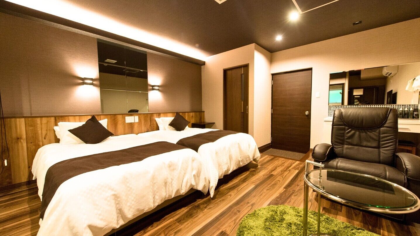 Habitación de hotel con dos camas, un sillón de cuero, una mesita y un espejo.