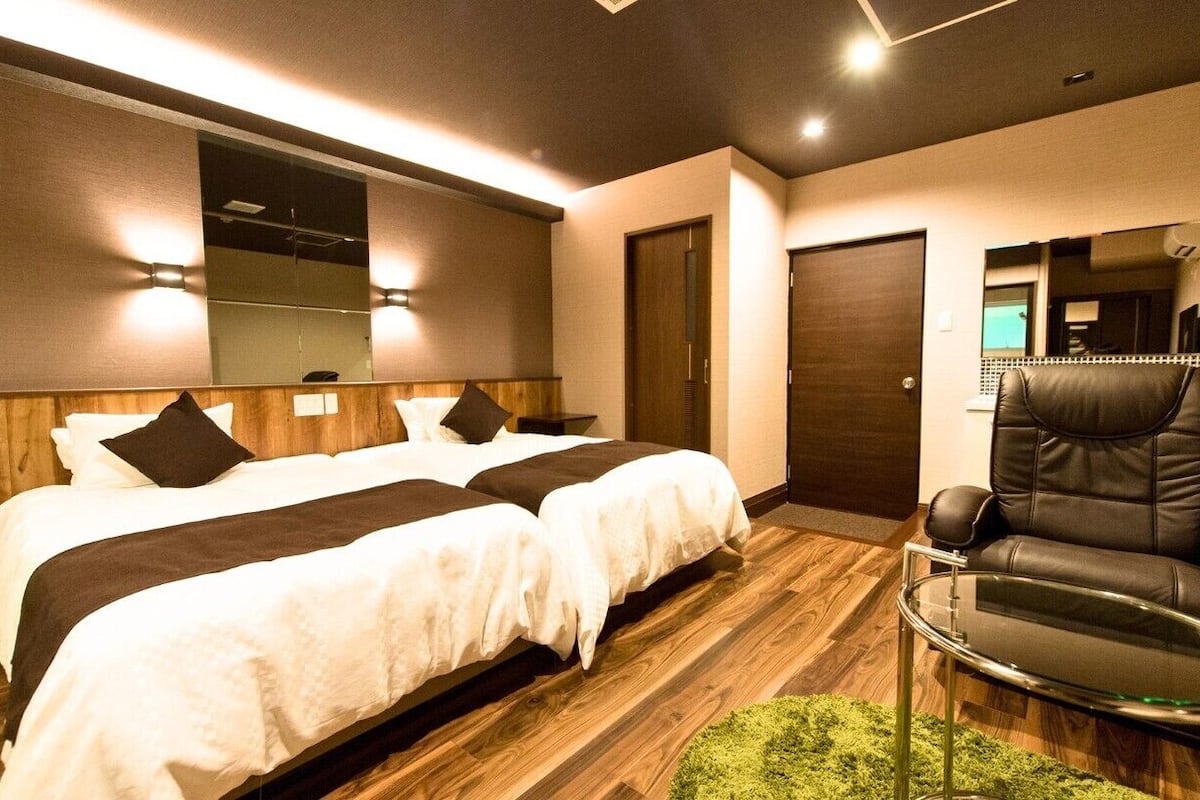 Habitación de hotel con dos camas, un sillón de cuero, una mesita y un espejo.