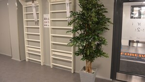 A hallway with white metal shelving units, a potted plant, and a door with a sign. - Forenom Aparthotel Raahe (Raahe)