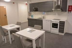 A modern kitchen with white and grey cabinetry, a built-in microwave, a sink, and a stove. There are two white tables with chairs, and a fire extinguisher is mounted on the wall.