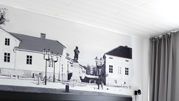 A hotel room with a bed, a headboard with a cityscape mural, and a window with curtains. - Forenom Aparthotel Raahe (Raahe)