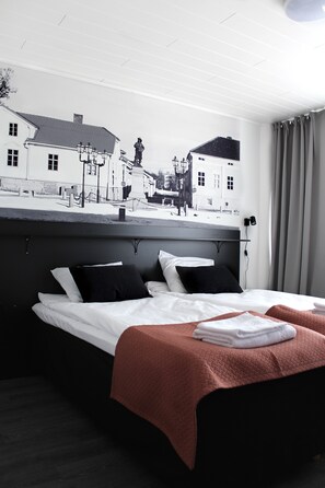 A hotel room with a bed, a headboard with a cityscape mural, and a window with curtains.
