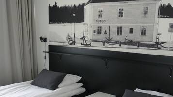 A hotel room with two beds, a headboard, a small bedside table, and a painting of a house on the wall.