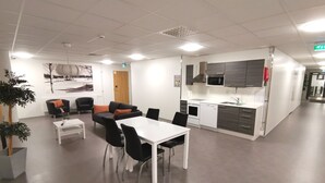 A modern kitchen with white appliances, a dining area with a white table and black chairs, and a seating area with black and orange chairs. - Forenom Aparthotel Raahe (Raahe)