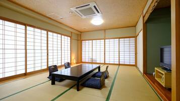 A traditional Japanese room with tatami flooring, a low table, chairs, and a television.