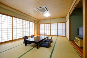 A traditional Japanese room with tatami flooring, a low table, chairs, and a television. - Hanasen (Yufu)