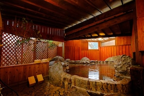 Uma cabana de madeira com uma banheira de pedra, bancos de madeira e um cercado de madeira.