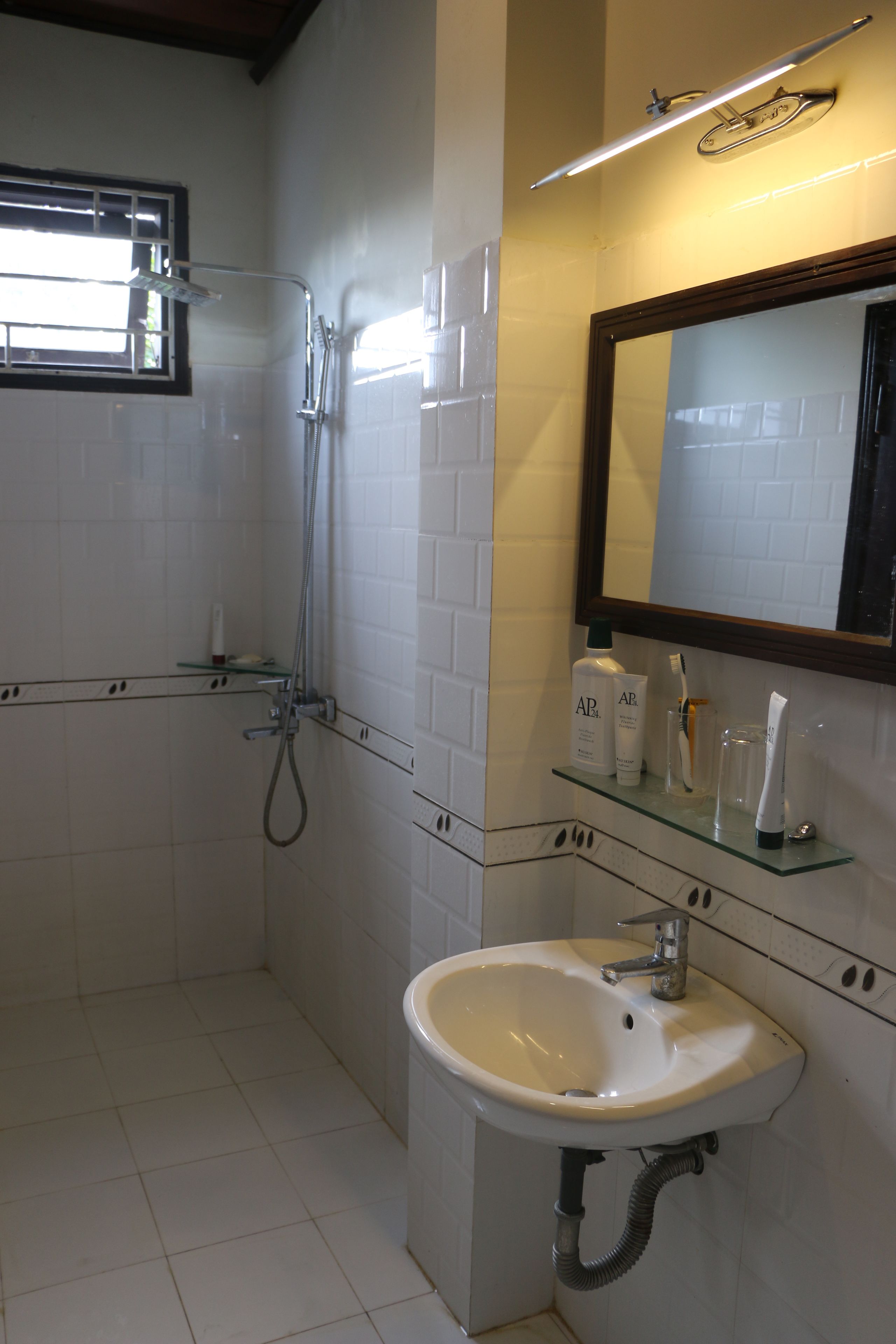 A bathroom with a white sink, mirror, and shower. There are toiletries on the shelf.