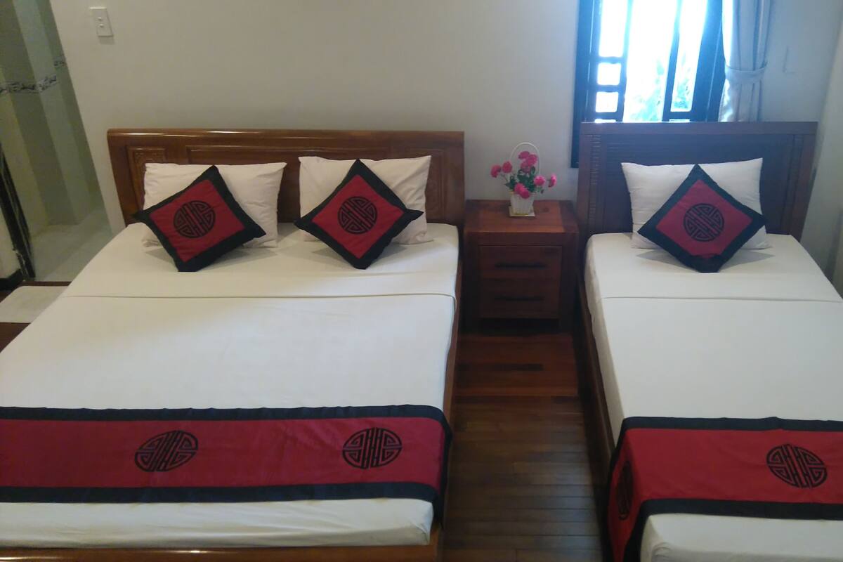 Two twin beds with matching red and black bedspreads, white pillows, and a wooden nightstand with a vase of flowers between them.