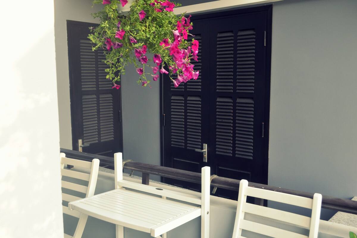 A white table and chairs set against a wall with two black doors and a hanging flower arrangement.