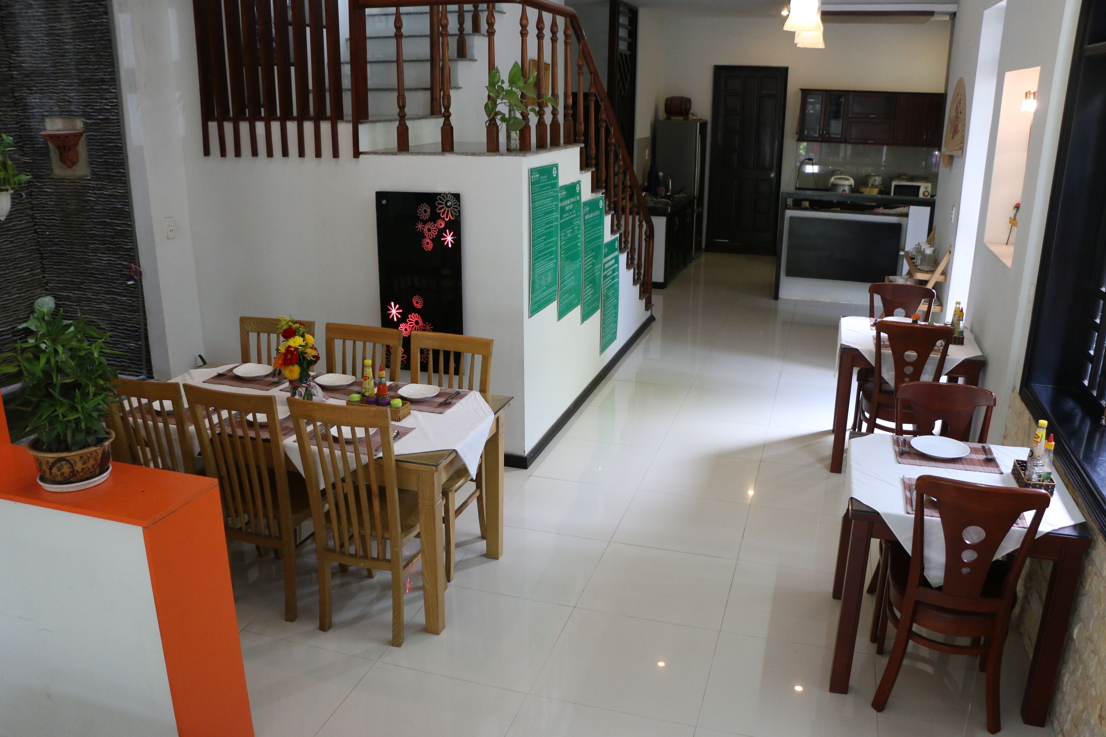 A dining area with wooden chairs and a table, a kitchen with dark cabinets, and a staircase with wooden railings.