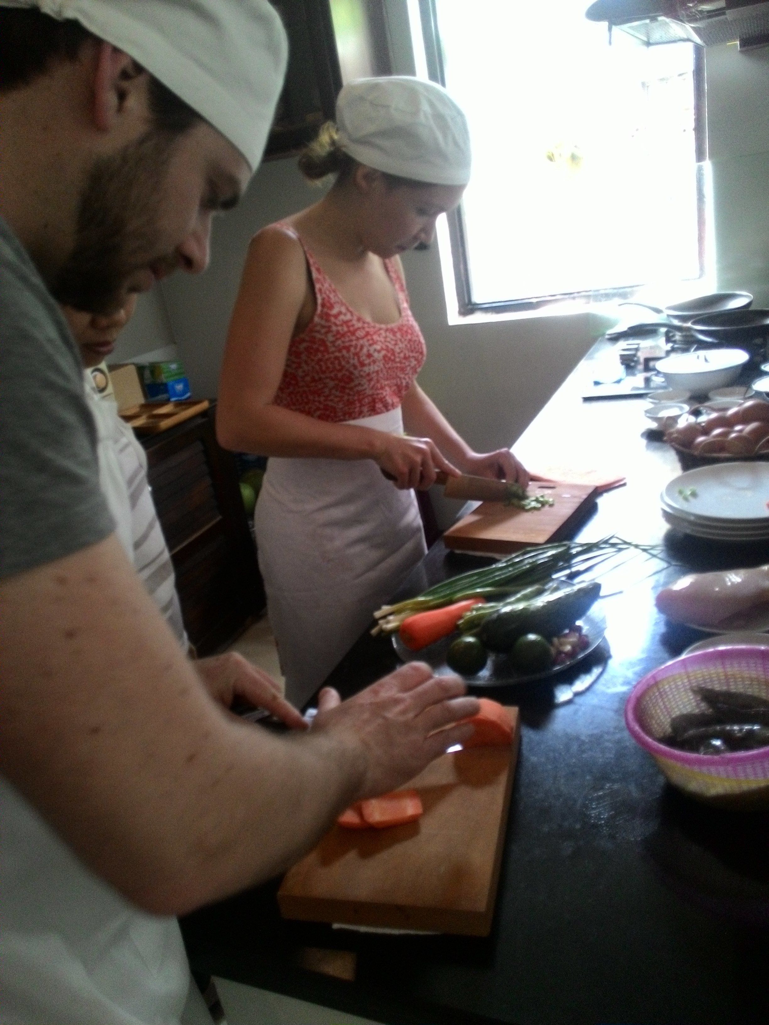 A kitchen with a cutting board, vegetables, and a person chopping.