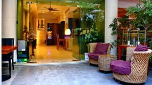 A hotel lobby with a glass entrance, wicker furniture, and indoor plants. - East Suites (Pattaya)