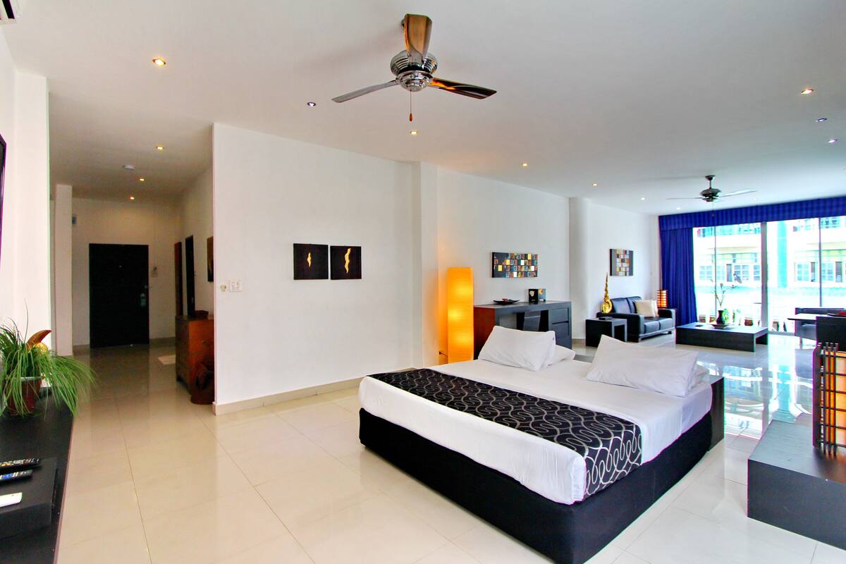 A modern hotel room with a large bed, a desk, a chair, and a ceiling fan.