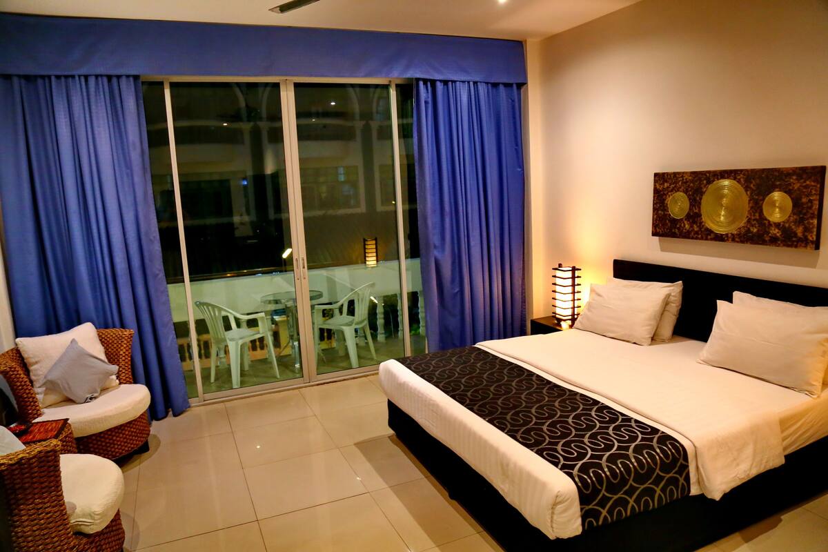 A hotel room with a bed, a chair, a table, and a view through a glass door.
