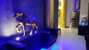 A modern lobby with a blue-lit horse sculpture on a platform, a staircase with a yellow pillar, and a small owl sculpture on a pedestal. - East Suites (Pattaya)