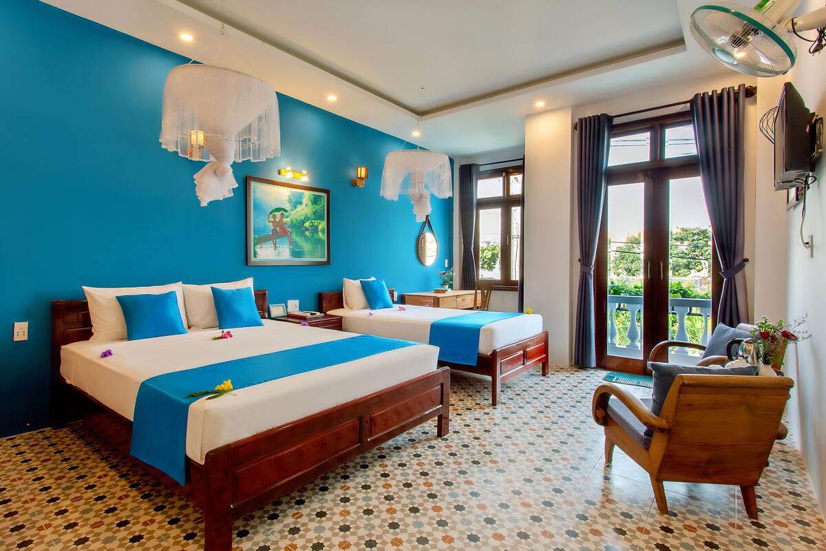 A hotel room with two beds, a wooden chair, a desk, and a balcony with a view.