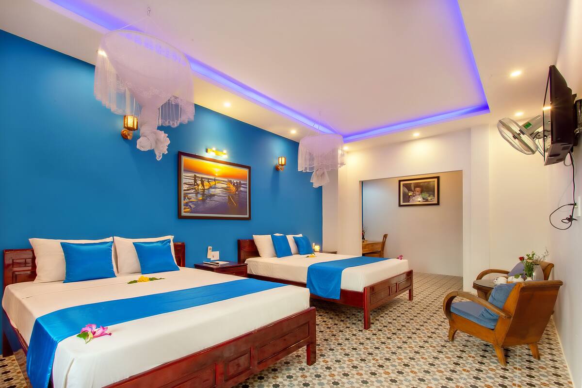 A hotel room with two beds, a wooden chair, a small table, and a TV mounted on the wall.