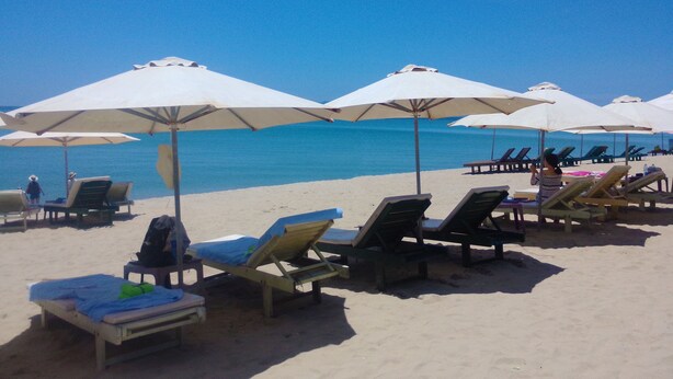 A beach with sun loungers and umbrellas, a clear blue sky, and the ocean in the background. - Lang Dong An Bang (Da Nang)