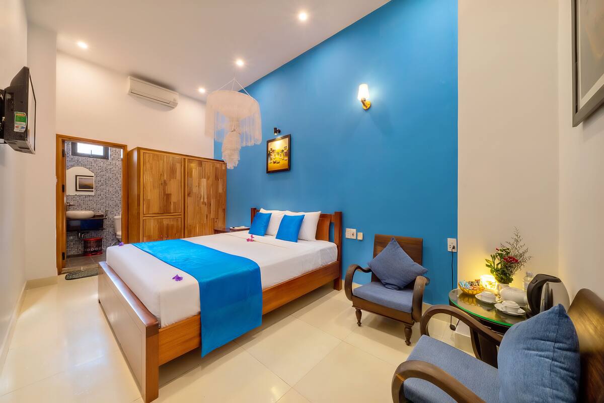 A bedroom with a bed, a chair, a small table with a lamp, and a wall-mounted picture.