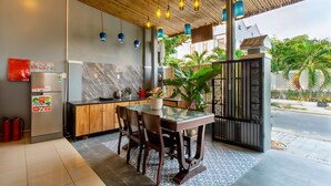 A modern kitchen with a wooden ceiling, hanging pendant lights, a marble backsplash, and a glass-top dining table with chairs. - Lang Dong An Bang (Da Nang)
