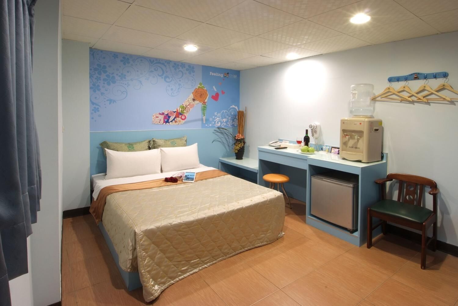 A hotel room with a bed, a desk, a chair, a small refrigerator, and a wall decoration.