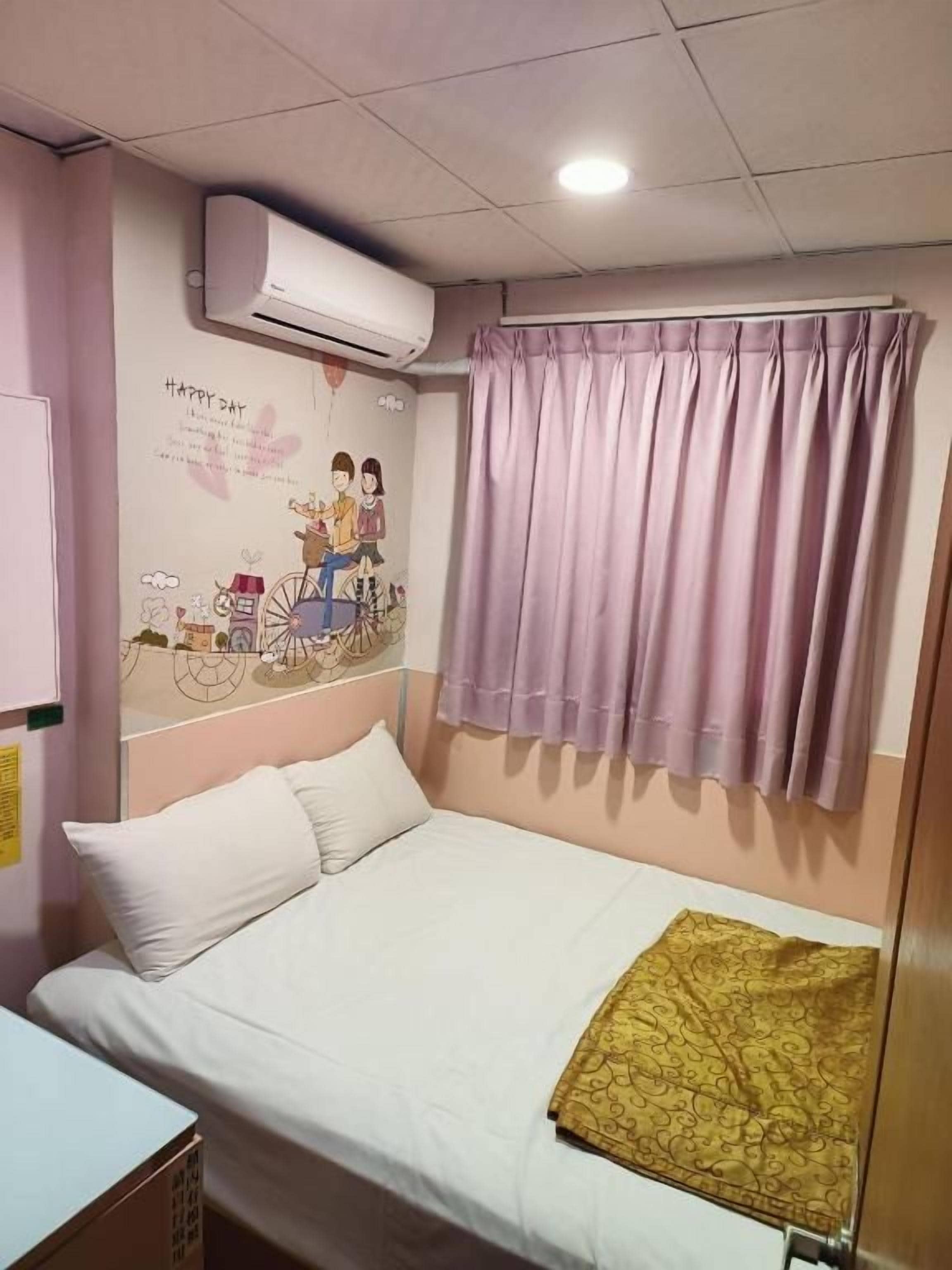 A single bed with a white mattress and pillows, a small bedside table, a wall-mounted air conditioner, and a window with purple curtains.