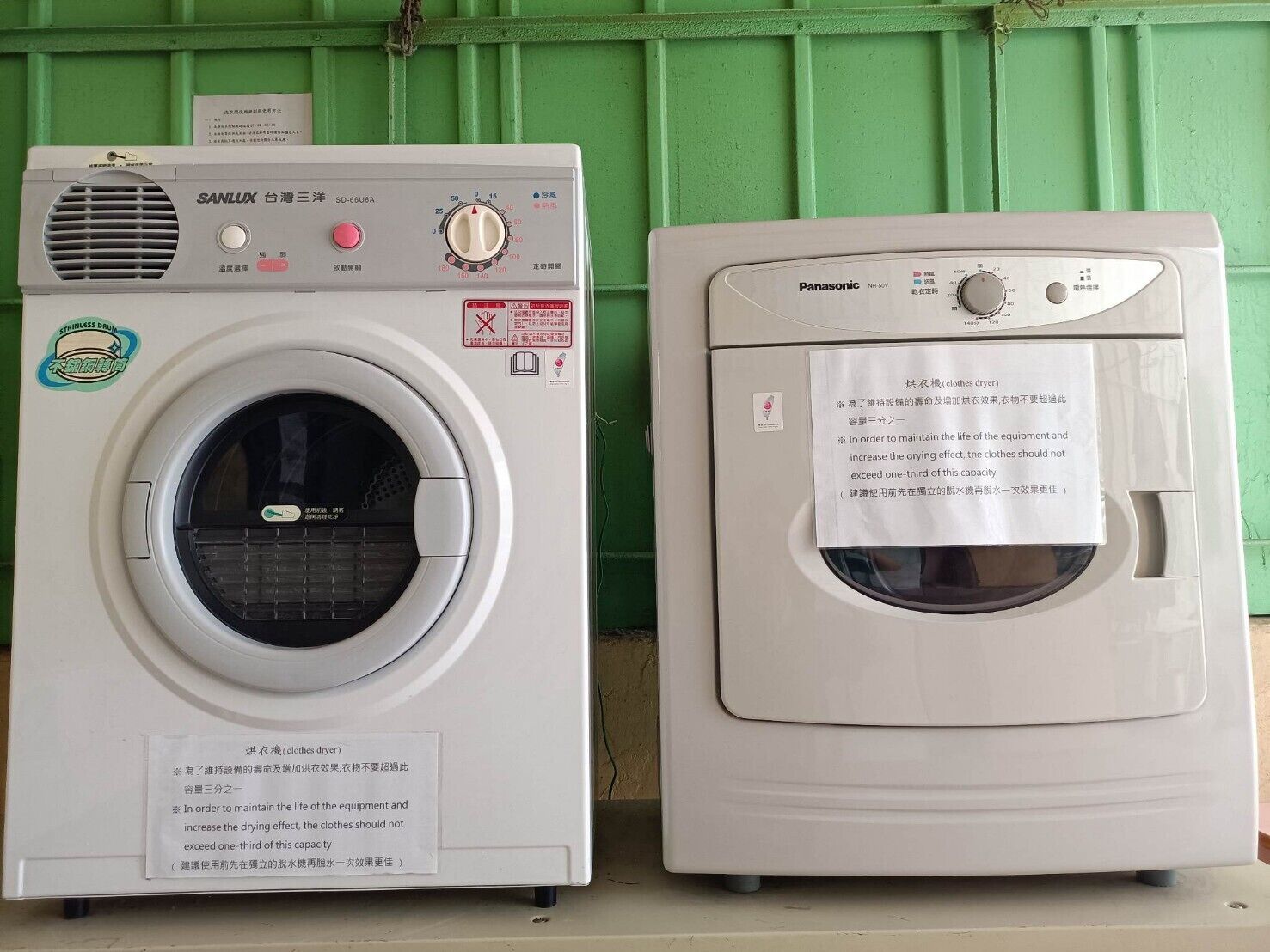 Two front-loading washing machines, one SANLUX and one Panasonic, with visible control panels and safety instructions.