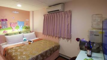 A hotel room with a bed, a desk with a water dispenser, a bottle of alcohol, and a plate with fruits.
