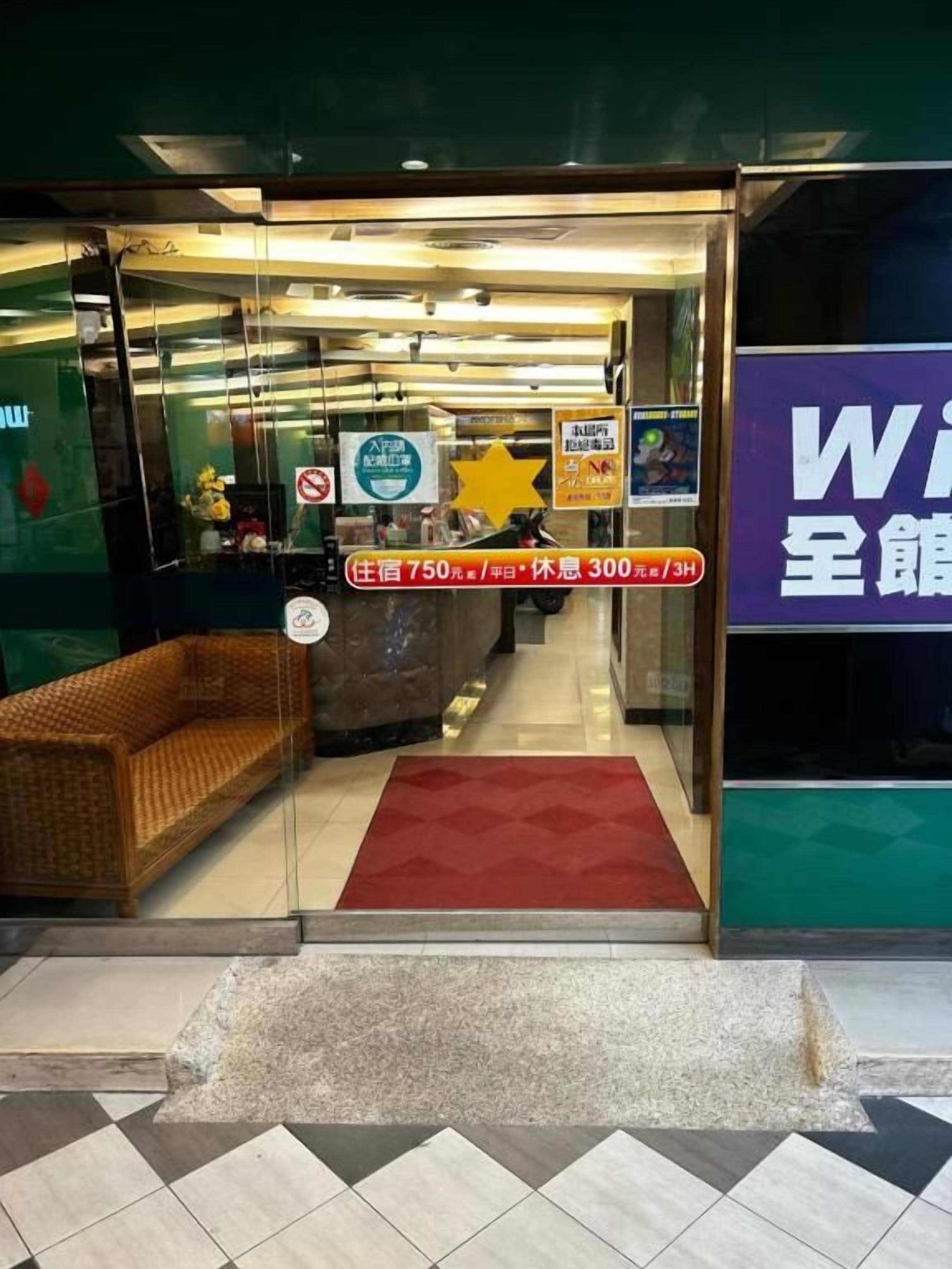 A hotel entrance with a glass door, a red carpet, and a wicker sofa outside.