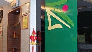 A reception area with a green wall, a wooden reception desk, and traditional Chinese decorations. - Tong Bing Express (Hsinchu)