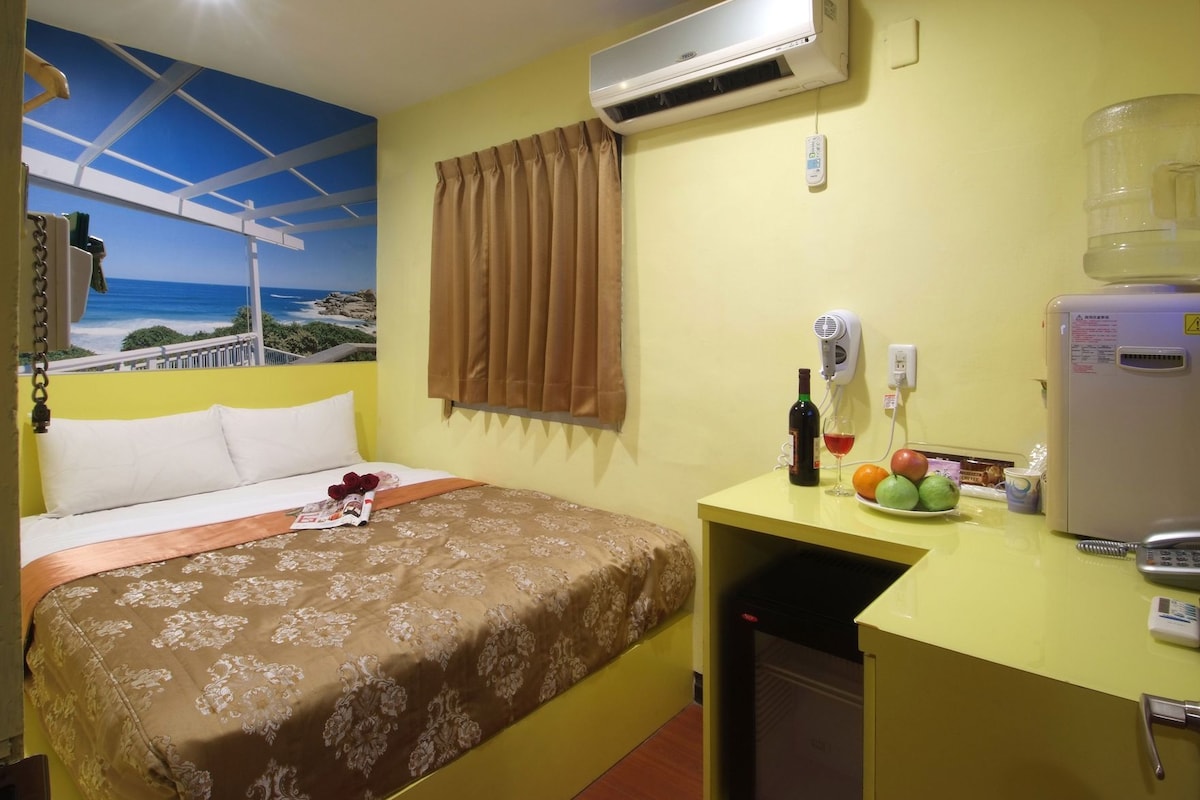 A hotel room with a bed, a desk with a water dispenser, a hairdryer, and a refrigerator.