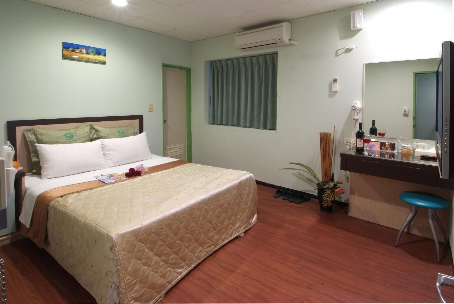 A hotel room with a bed, a desk with a mirror, a small plant, and a window with curtains.
