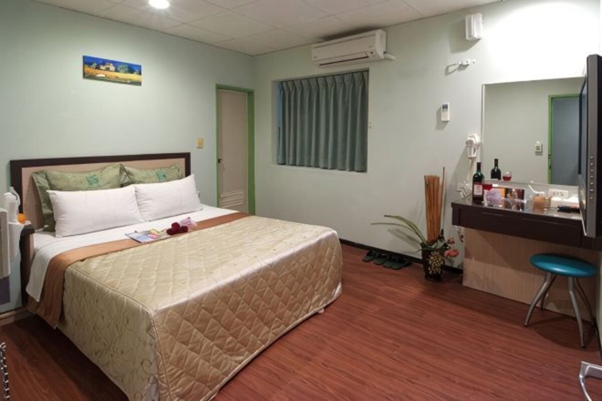 Una camera d'albergo con un letto, una scrivania con uno specchio, una sedia e un comodino con articoli da toilette.