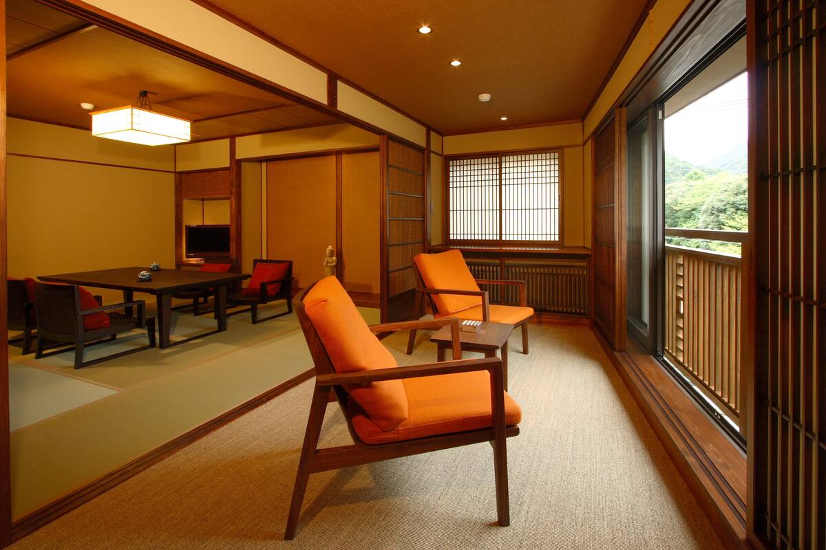 Une pièce de style japonais traditionnel, avec un sol recouvert de tatamis, une petite table basse entourée de coussins et une porte coulissante donnant sur un balcon avec vue sur la verdure.