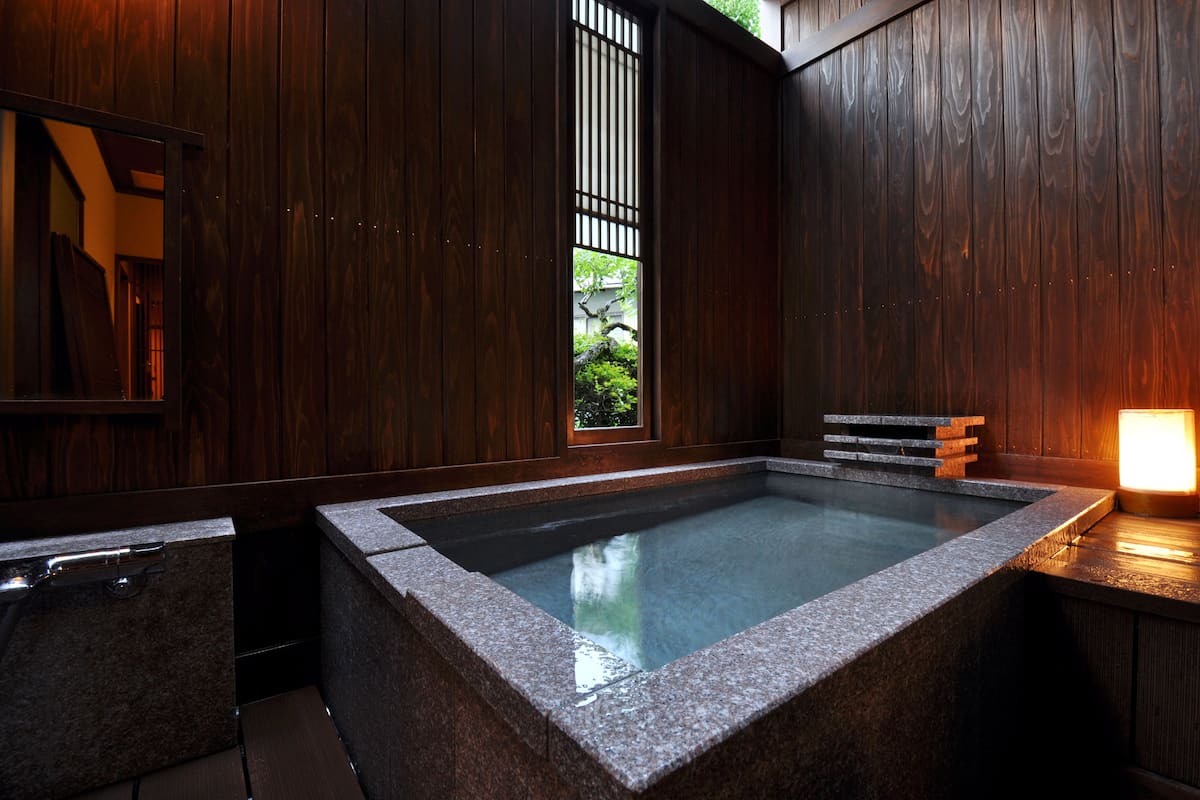 Un onsen japonais traditionnel, avec un bain en pierre, des murs en bois et une vue sur la verdure environnante.