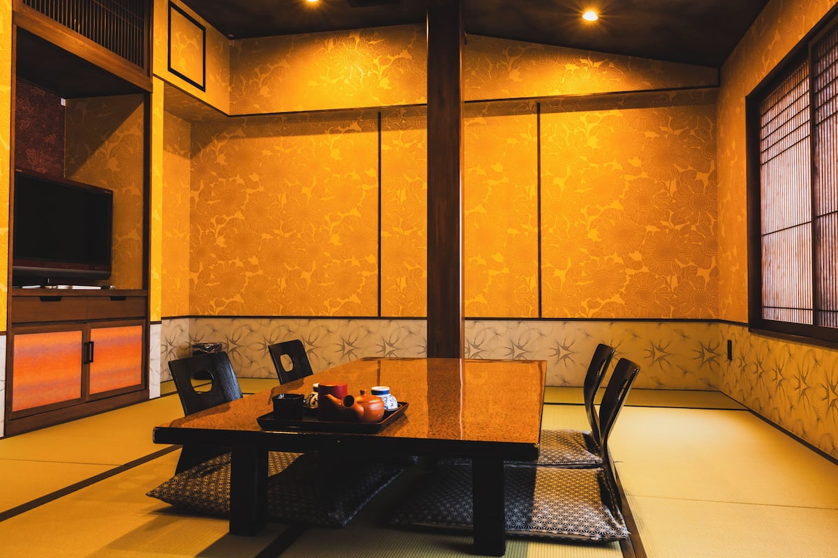 Une pièce de style japonais traditionnel, avec un sol recouvert de tatamis, une petite table sur laquelle se trouve un plateau contenant divers objets, et un téléviseur placé sur le côté gauche.