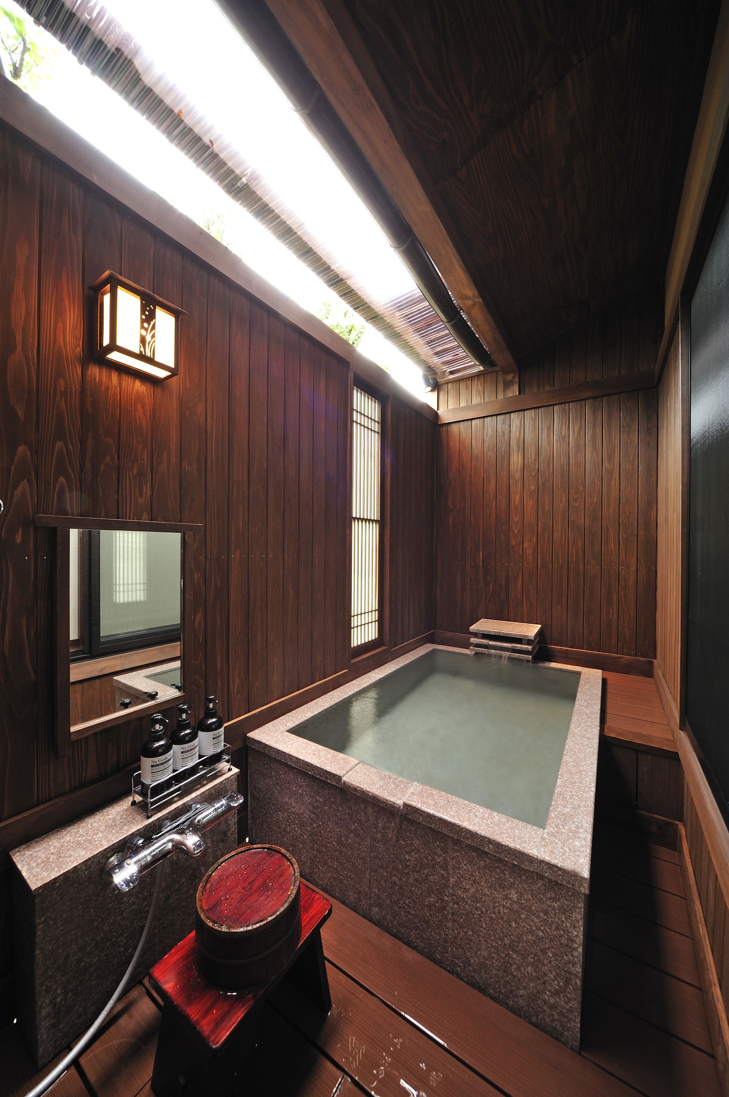 A traditional Japanese onsen with a wooden interior, a hot spring bath, a wooden bench, and a small table with a bottle.