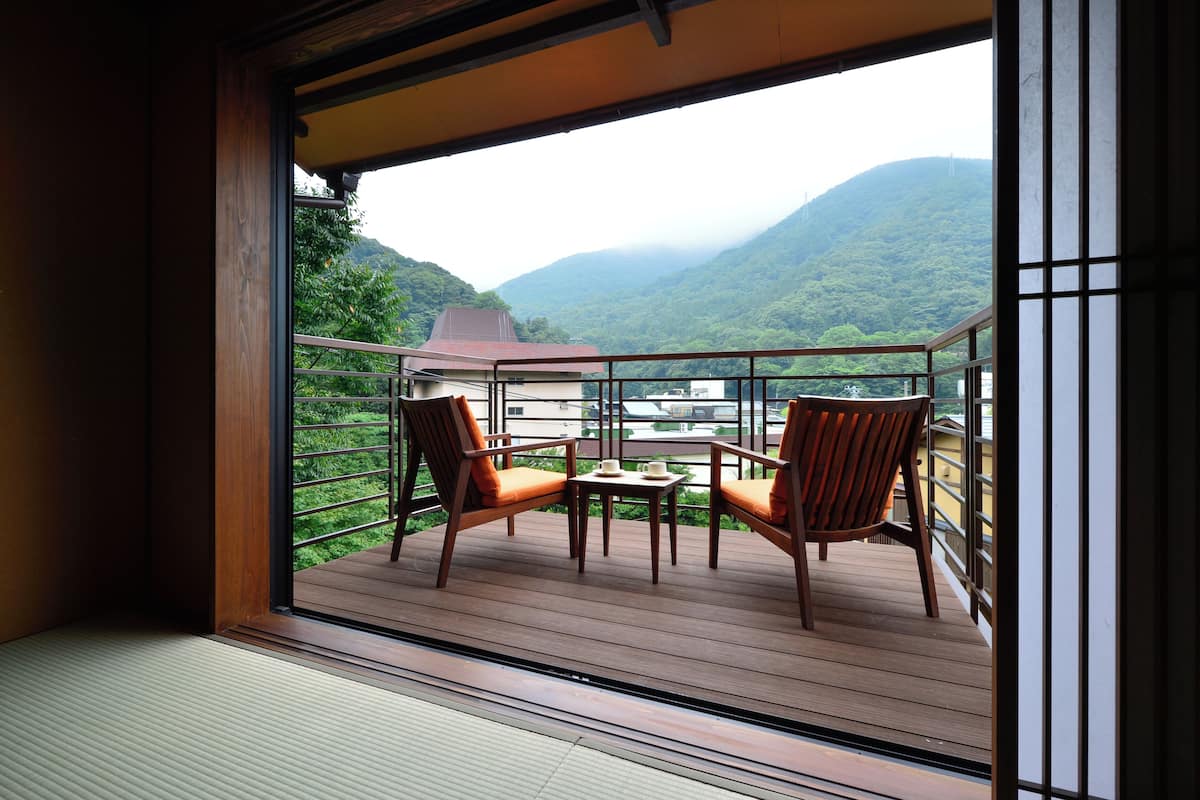 Un balcon doté d’un plancher en bois, de deux chaises, d’une petite table et offrant une vue sur une montagne.