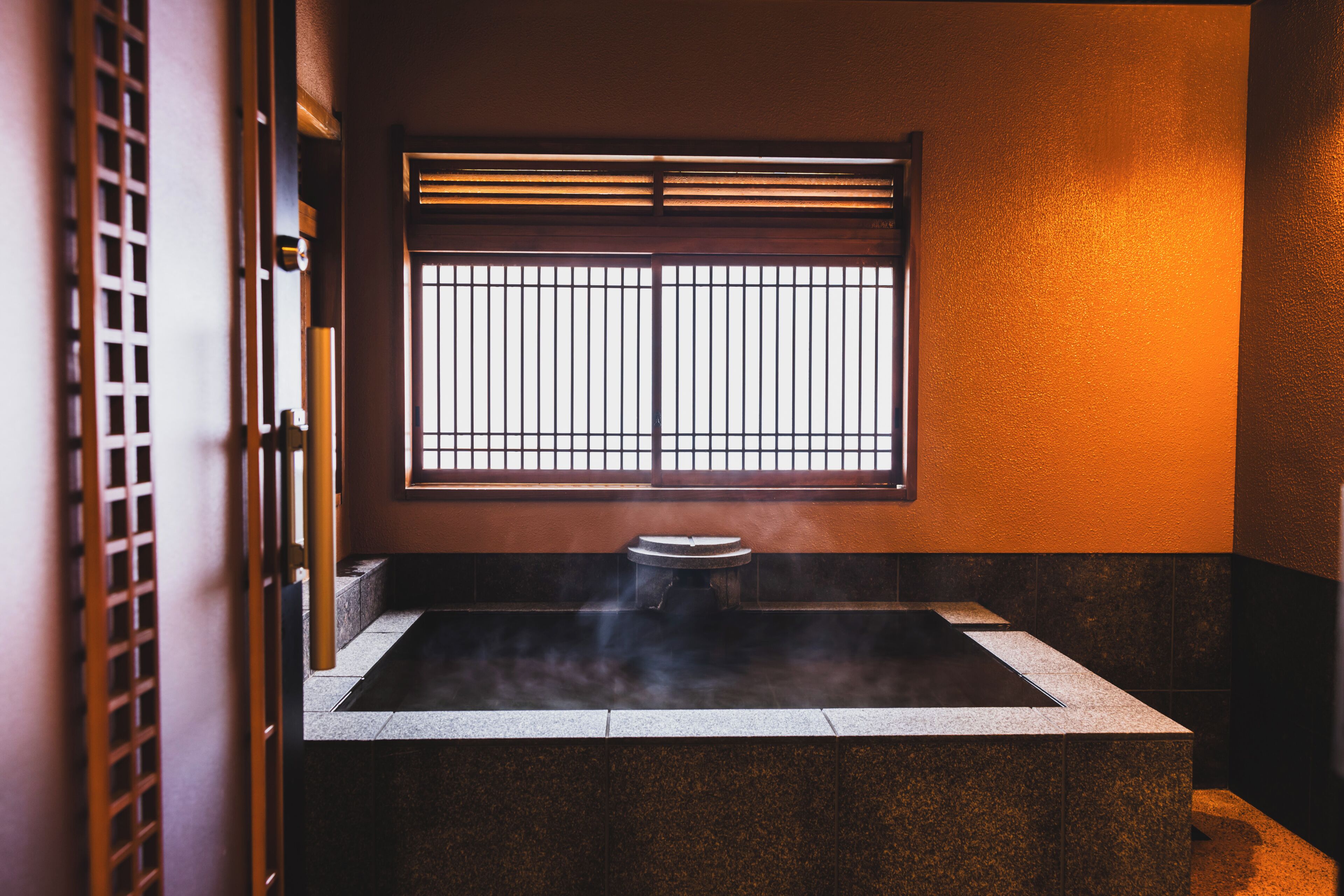 Ein traditionelles japanisches Onsen mit Fenster, gefliesten Wänden und einer Holztür.