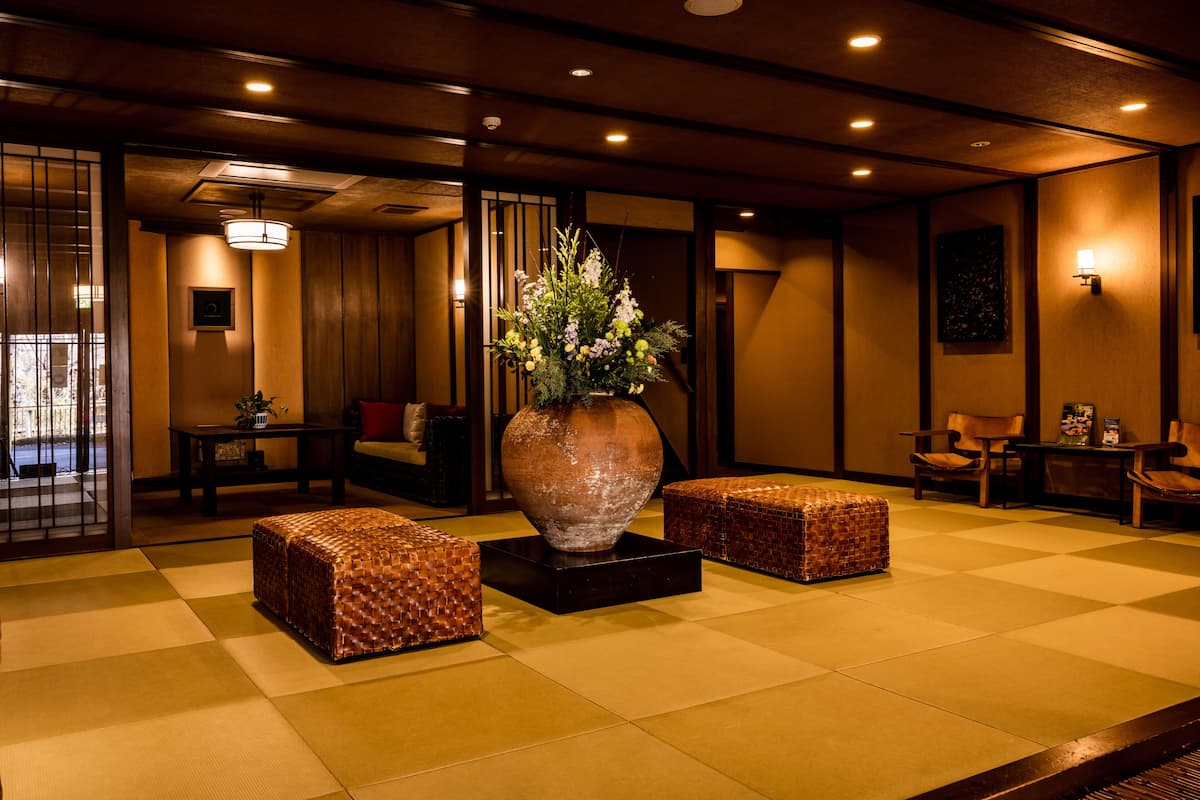 Un hall d’entrée de style japonais traditionnel, avec un sol recouvert de tatamis, un grand vase rempli de fleurs et des meubles en bois.