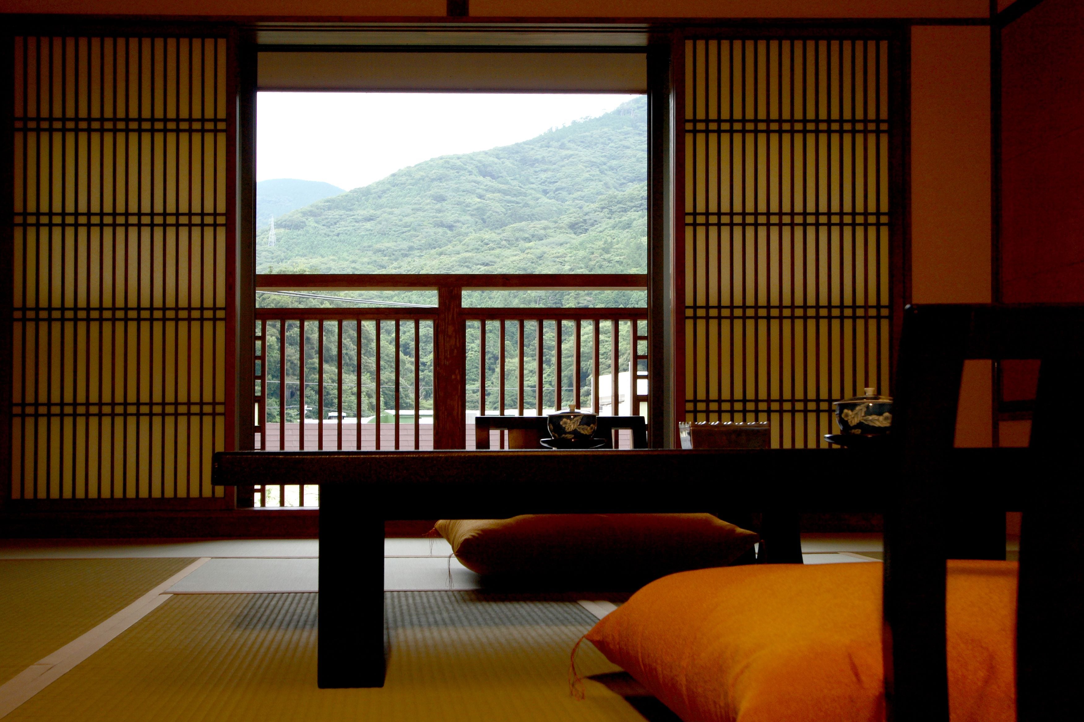 A traditional Japanese room with tatami flooring, a low table, and a view of a mountainous landscape through shoji screens.